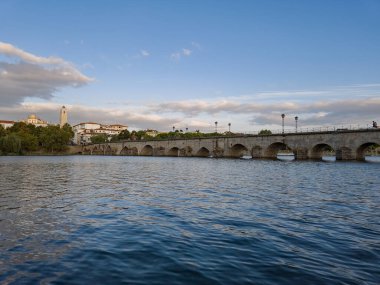 The historic granite Old Bridge crosses the Tua River in Mirandela, Portugal, with the cityscape and iconic tower behind. This scenic pedestrian landmark blends heritage and beauty in northern Portugal.