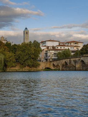 The historic granite Old Bridge crosses the Tua River in Mirandela, Portugal, with the cityscape and iconic tower behind. This scenic pedestrian landmark blends heritage and beauty in northern Portugal.