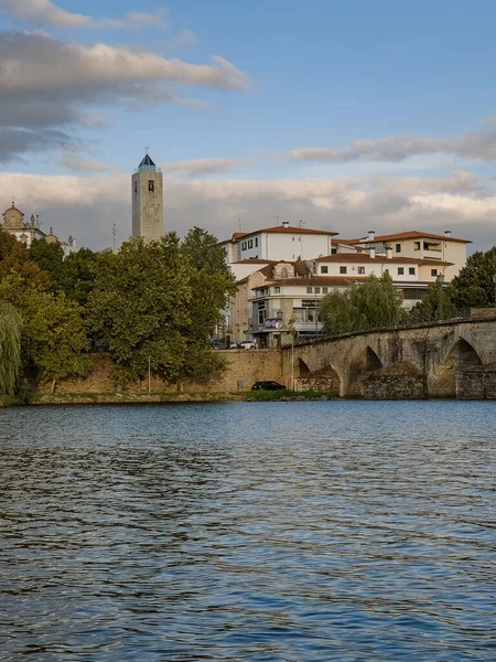 The historic granite Old Bridge crosses the Tua River in Mirandela, Portugal, with the cityscape and iconic tower behind. This scenic pedestrian landmark blends heritage and beauty in northern Portugal.