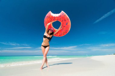 Gülümseyen pembe şapkalı güzel esmer kadın büyük bir şişme tüp üzerinde Karayip Denizi kıyısında yaz güneşli gün düzenliyor