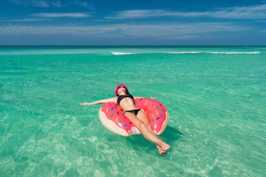 Pembe şapkalı mutlu güzel esmer kadın büyük bir şişme tüp Karayip Denizi kıyısında yaz güneşli bir günde yatıyor