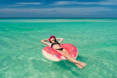 Güzel esmer kadın pembe şapka ve siyah mayo büyük bir şişme tüp Karayip Denizi kıyısında yaz güneşli bir günde yatıyor