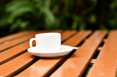 Beyaz kahve fincanı çay tabağında, tahta masada kaşık, sakin bir sabah sahnesi.