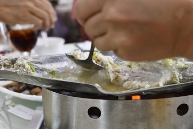 Buğulanmış balık filetosu, çorba ve sebzelerle ızgara tepside kepçeleniyor. Elleri, günlük yemek atmosferiyle birlikte ortak yemek servisi yapıyor.