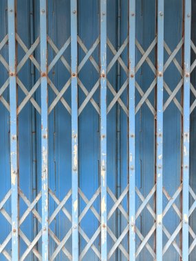 Çapraz kafes desenli, mavi metal kapılı ve boyalı, kentsel dokuyu ve endüstriyel nostaljiyi çağrıştırıyor.