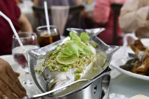 Limonlu, sarımsaklı ve bitkisel garnitürlü haşlanmış balık. Yoğun bir restoranda metal tabakta servis ediliyor. Taze deniz ürünleri ve canlı turunçgil aroması.