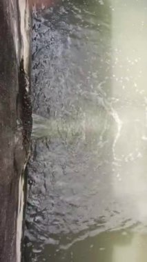 Su, betondan su birikintisine akar. Dalgalanmalar yaratır. Gri su yüzeyinde kaya yansıması oluşur.