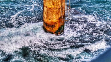 Güçlü okyanus dalgaları paslı bir petrol kuyusu destek yapısına çarpıyor. Endüstriyel ya da endüstriyel olarak uygun dramatik bir deniz manzarası yaratıyor..