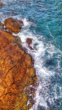 Turkuaz okyanus suyu, kayalık bir kıyı şeridine çarptığında köpüklü beyaz dalgalar yaratır. Bu da dramatik bir kıyı sahnesi oluşturur. Yolculuk ve seyahat için mükemmel..
