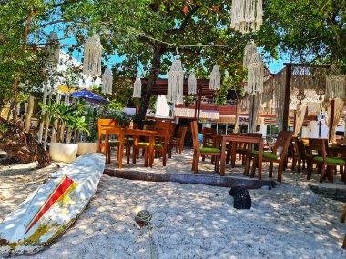 Lombok, Endonezya 5 Ağustos 2024. Gili Trawangan. Tahta masalar, beyaz kumlar, sörf tahtası ve makrome dekorla rahatlatıcı bir plaj kafesi seyahat ve yaşam tarzı için mükemmel bir ortam yaratıyor..