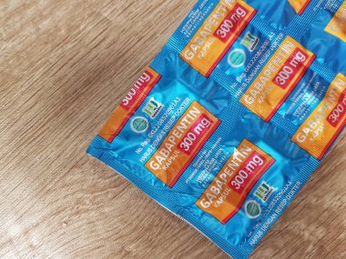 Bekasi, Endonezya 21 Nisan 2024. Gabapentin kapsüllerini içeren mavi ve turuncu su toplayıcıları ahşap arka planda sergileniyor ve ilaç kullanımına ilişkin sağlık hizmetleri görüntülerini sunuyor..