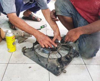 Bekasi, Endonezya 21 Nisan 2024. İki tamirci bir araba radyatörü vantilatörünü delici yağ ve kapalı alanda yakın mesafeden gösterilen bir tornavida kullanarak tamir ediyor. Otomotiv tamiri için kullanışlı veya.
