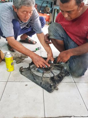 Bekasi, Endonezya 21 Nisan 2024. İki tamirci, otomotiv tamiri ve bakım için ideal bir atölye ortamında bir araba soğutma vantilatörünü tamir ediyor..