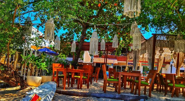 Lombok, Endonezya 5 Ağustos 2024. Gili Trawangan. Kumlu bir sahildeki açık hava restoranını davet etmek ahşap masalar, makrome fenerler ve bereketli ağaç örtüsü seyahat ve etkinlik promosyonları için harika..
