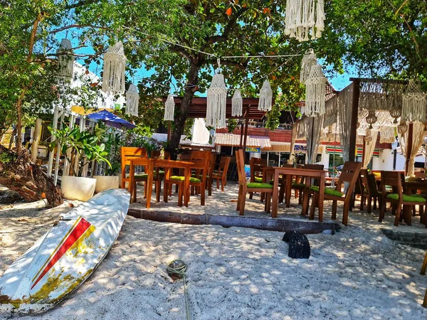 Lombok, Endonezya 5 Ağustos 2024. Gili Trawangan. Tahta masalar, beyaz kumlar, sörf tahtası ve makrome dekorla rahatlatıcı bir plaj kafesi seyahat ve yaşam tarzı için mükemmel bir ortam yaratıyor..