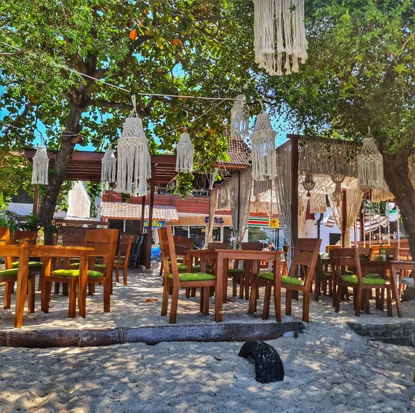 Lombok, Endonezya 5 Ağustos 2024. Gili Trawangan. Büyüleyici açık hava kafe ahşap masalar ve kumlu bir sahildeki ağaçların arasında makrome avizeler içerir. Bohem tarzını sergilemek için mükemmeldir..