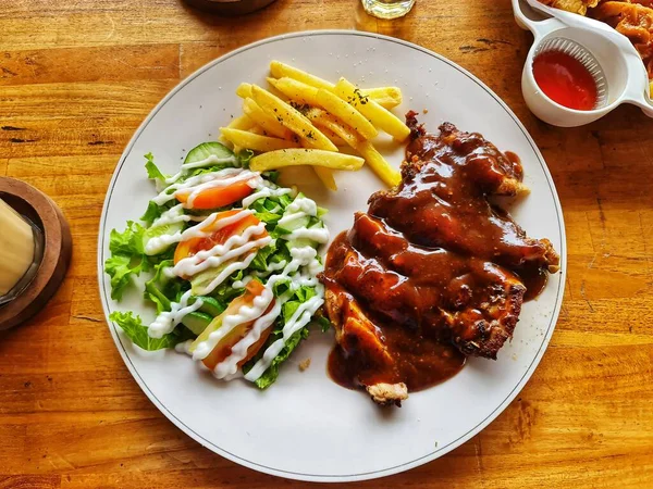 Sos soslu lezzetli bir tavuk bifteği, yanında taze salata ve altın patates kızartması servis edilir. Restoran ve yemek blogu içeriği için mükemmeldir..