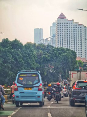 Jakarta, Endonezya 12 Nisan 2025. Araçlar modern binalar ve yemyeşil ağaçlarla dolu işlek bir şehir caddesinde dolaşarak seyahat ve şehir hayatı tasvirleri için ideal bir şehir atmosferi yaratıyorlar..