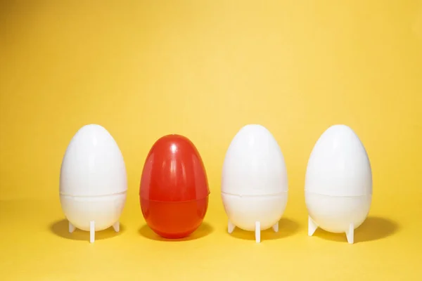 Difference concept. Four eggs on yellow. One red and three white plastic eggs on yellow background