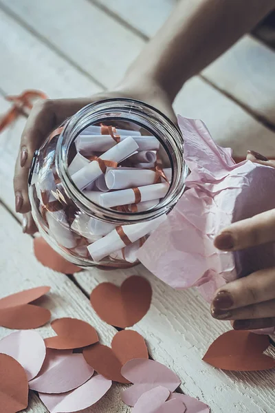 Lover's day. Hand opening glass jar or date Jar with desires or wishes. Red paper hearts at background.