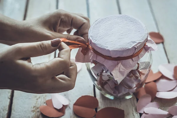 Lover's day. Hand opening glass jar or date Jar with desires or wishes. Red paper hearts at background.