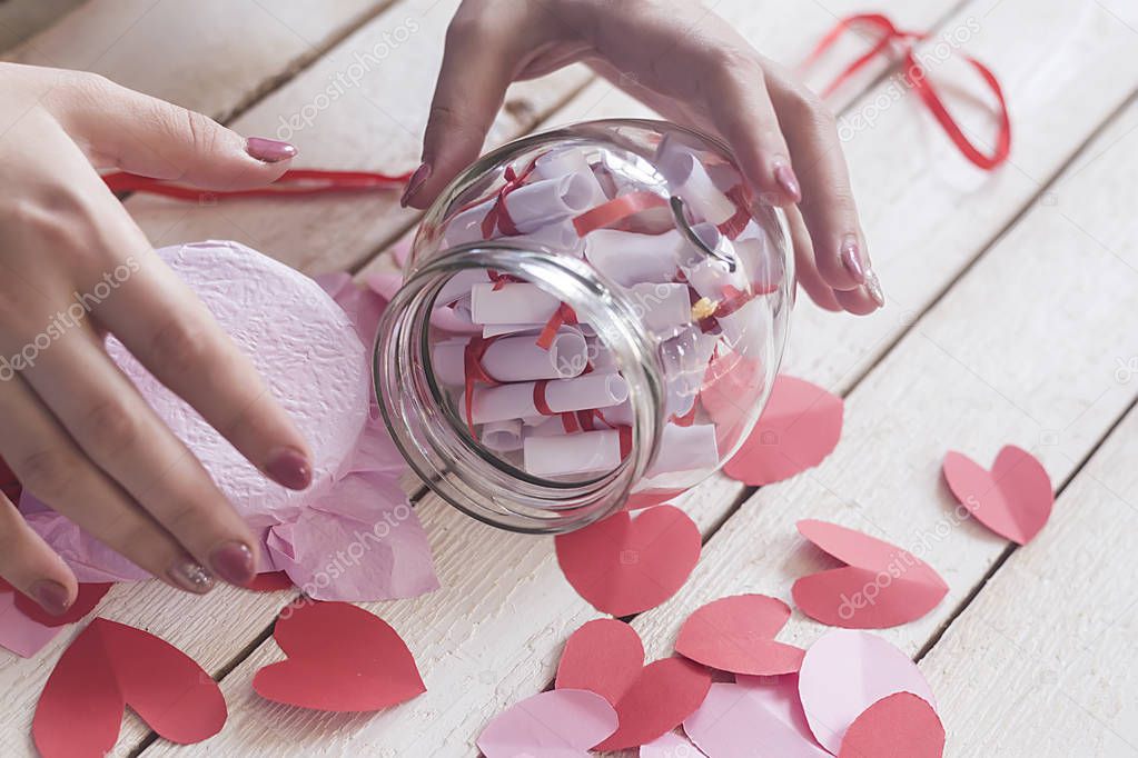 Lover's day. Hand opening glass jar or date Jar with desires or wishes. Red paper hearts at background.