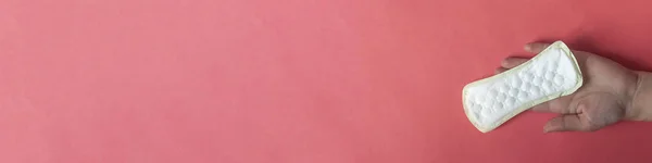 La mano de la mujer sosteniendo una toalla sanitaria sobre el fondo rosa. Una foto grande del tamaño de una pancarta de una mano sosteniendo una almohadilla de higiene femenina — Foto de Stock