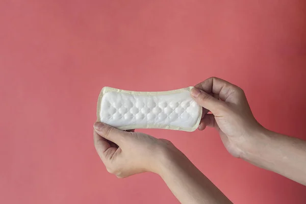 Una toalla sanitaria blanca en las manos de la mujer sobre un fondo rosa con espacio para copiar. Artículo absorbente para mujeres días especiales. Concepto de higiene y salud . — Foto de Stock