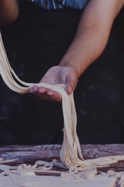 Genç ev hanımı mutfakta ev yapımı makarna hazırlıyor. Kadınların elleri makarna pişirmek için uzun hamur şeritlerini tutuyor..
