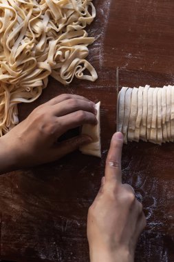 Genç ev hanımı mutfakta ev yapımı makarna hazırlıyor. Makarna pişirmek için uzun hamurlu şerit kesen kadın..
