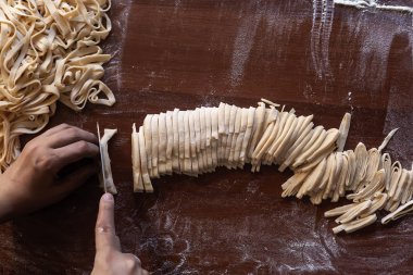 Genç ev hanımı mutfakta ev yapımı makarna hazırlıyor. Makarna pişirmek için uzun hamurlu şerit kesen kadın..