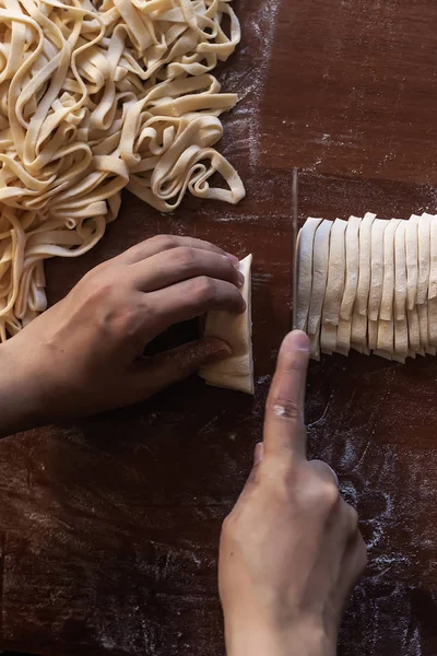 Genç ev hanımı mutfakta ev yapımı makarna hazırlıyor. Makarna pişirmek için uzun hamurlu şerit kesen kadın..