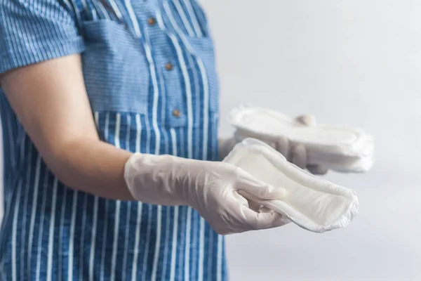 Productos de higiene femenina. Mujer con guantes médicos sosteniendo una pila de toallas sanitarias sobre fondo blanco. Concepto de días de período que muestra el ciclo menstrual femenino . — Foto de Stock