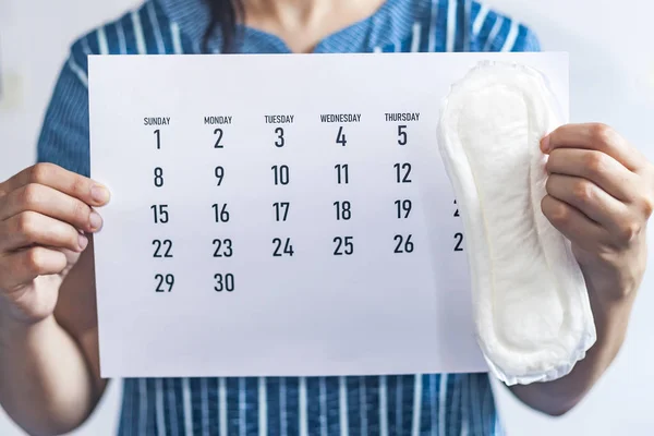 Woman holding monthly calendar and sanitary pads. Menstruation cycle calendar. Women health concept. Period days concept showing feminine menstrual cycle.