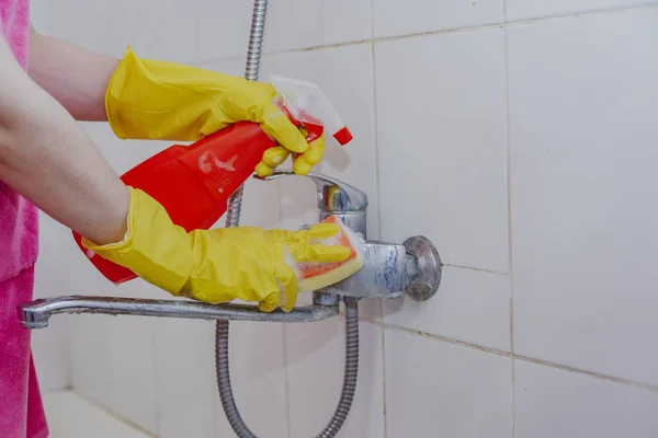 Housewife cleaning bathroom tap and shower Tap. Maid in yellow protective gloves washing dirty bath tap. Hands of woman washing bath
