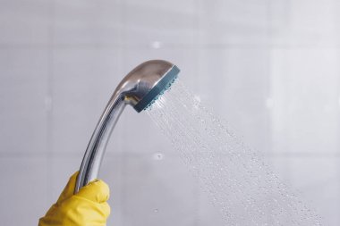 Lastik eldivenli bir kişi, akan suyla duş başlığı tutuyor. Banyoda akan su ile duş başını tutan sarı koruyucu eldiven kadınlar