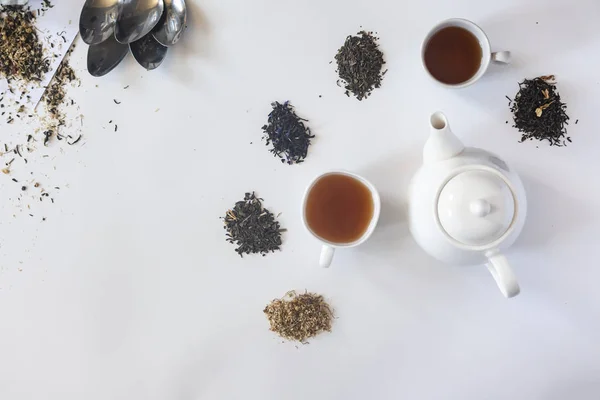 Tea set with white ceramic tea pot and other tea ingredients on the white. Flat lay view of various dried teas and teapot. View from above. Space for your text