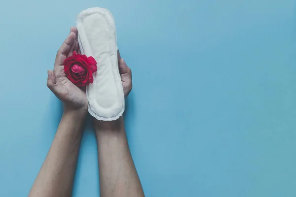 Female's hand holding sanitary napkins with red rose on it. Period days concept showing feminine menstrual cycle. Female's hygiene — Stock Photo, Image