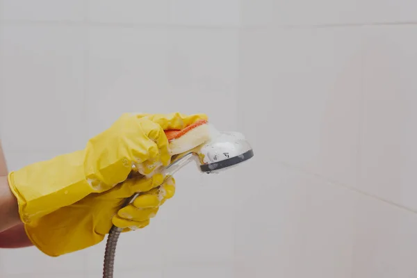 Mujer con guantes de goma limpiando el cabezal de ducha. Limpieza lavando cabezal metálico de la ducha. Limpieza de la ama de casa en el baño — Foto de Stock