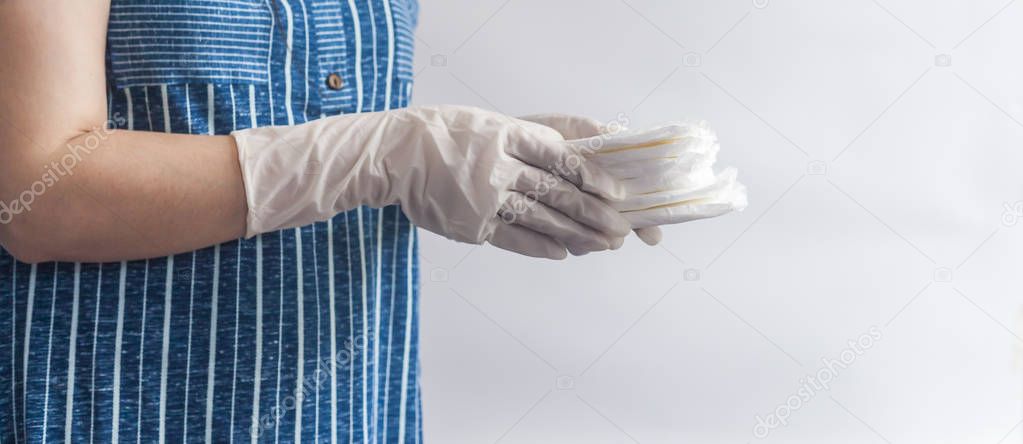 Female's hygiene products. Woman in medical gloves holding a stack of sanitary napkins against white background. Period days concept showing feminine menstrual cycle.