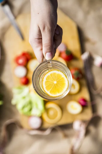 Woman's hand holding a glass of fresh lemon water — Stok fotoğraf