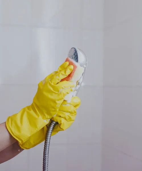 Mujer con guantes de goma limpiando el cabezal de ducha. Limpieza lavando cabezal metálico de la ducha. Limpieza de la ama de casa en el baño — Foto de Stock