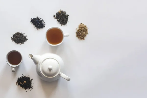 Set de té con tetera de cerámica blanca y otros ingredientes del té en el blanco. Vista plana de varios tés secos y tetera. Vista desde arriba. Espacio para tu texto — Foto de Stock