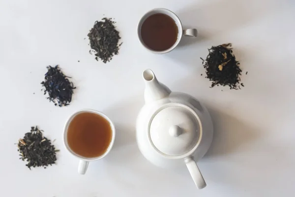 Set de té con tetera de cerámica blanca y otros ingredientes del té en el blanco. Vista plana de varios tés secos y tetera. Vista desde arriba. Espacio para tu texto — Foto de Stock