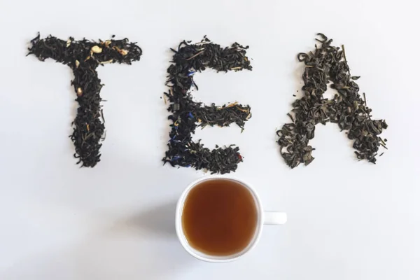 Słowo herbata wykonana z liści suchej herbaty i filiżankę czarnej herbaty — Zdjęcie stockowe