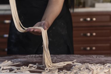 Genç ev hanımı mutfakta ev yapımı makarna hazırlıyor. Kadınların elleri makarna pişirmek için uzun hamur şeritlerini tutuyor..