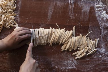 Genç ev hanımı mutfakta ev yapımı makarna hazırlıyor. Makarna pişirmek için uzun hamurlu şerit kesen kadın..