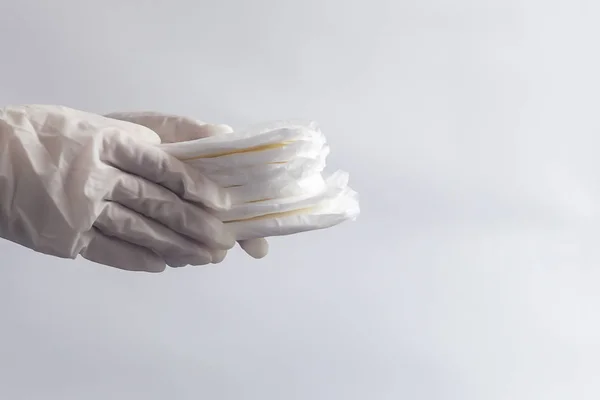 Productos de higiene femenina. Manos de mujer con guantes médicos sosteniendo una pila de toallas sanitarias sobre fondo blanco. Concepto de días de período que muestra el ciclo menstrual femenino . — Foto de Stock