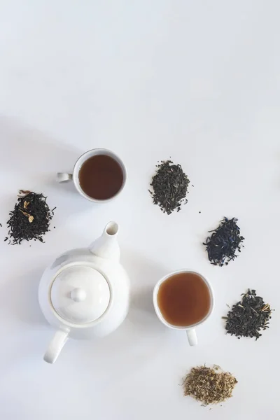 Conjunto de chá com panela de chá de cerâmica branca e outros ingredientes de chá no branco. Plana vista leigos de vários chás secos e bule. Vista de cima. Espaço para o seu texto — Fotografia de Stock
