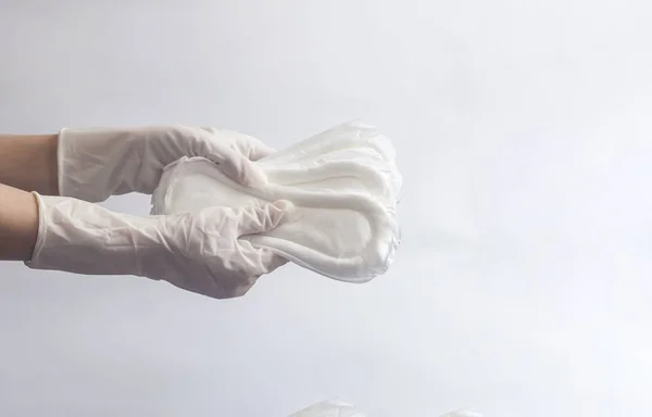 Productos de higiene femenina. Manos de mujer con guantes médicos sosteniendo una pila de toallas sanitarias sobre fondo blanco. Concepto de días de período que muestra el ciclo menstrual femenino . — Foto de Stock